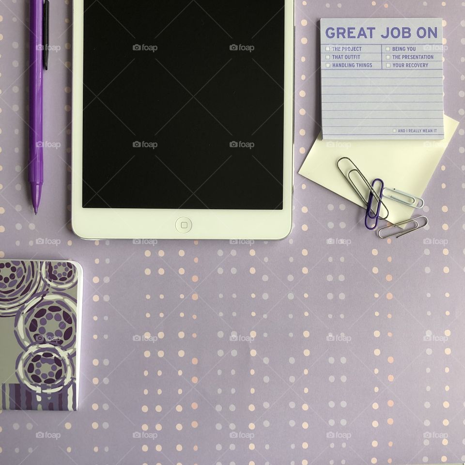 A flat lay of office supplies including technology and an iPad in a purple theme