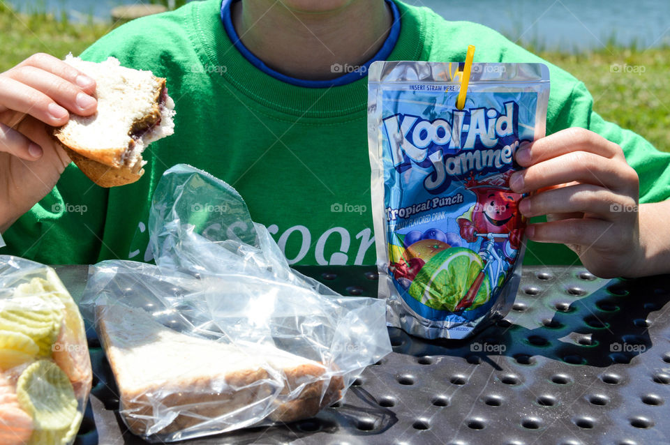 Young child eating lunch outdoors with a drink pouch