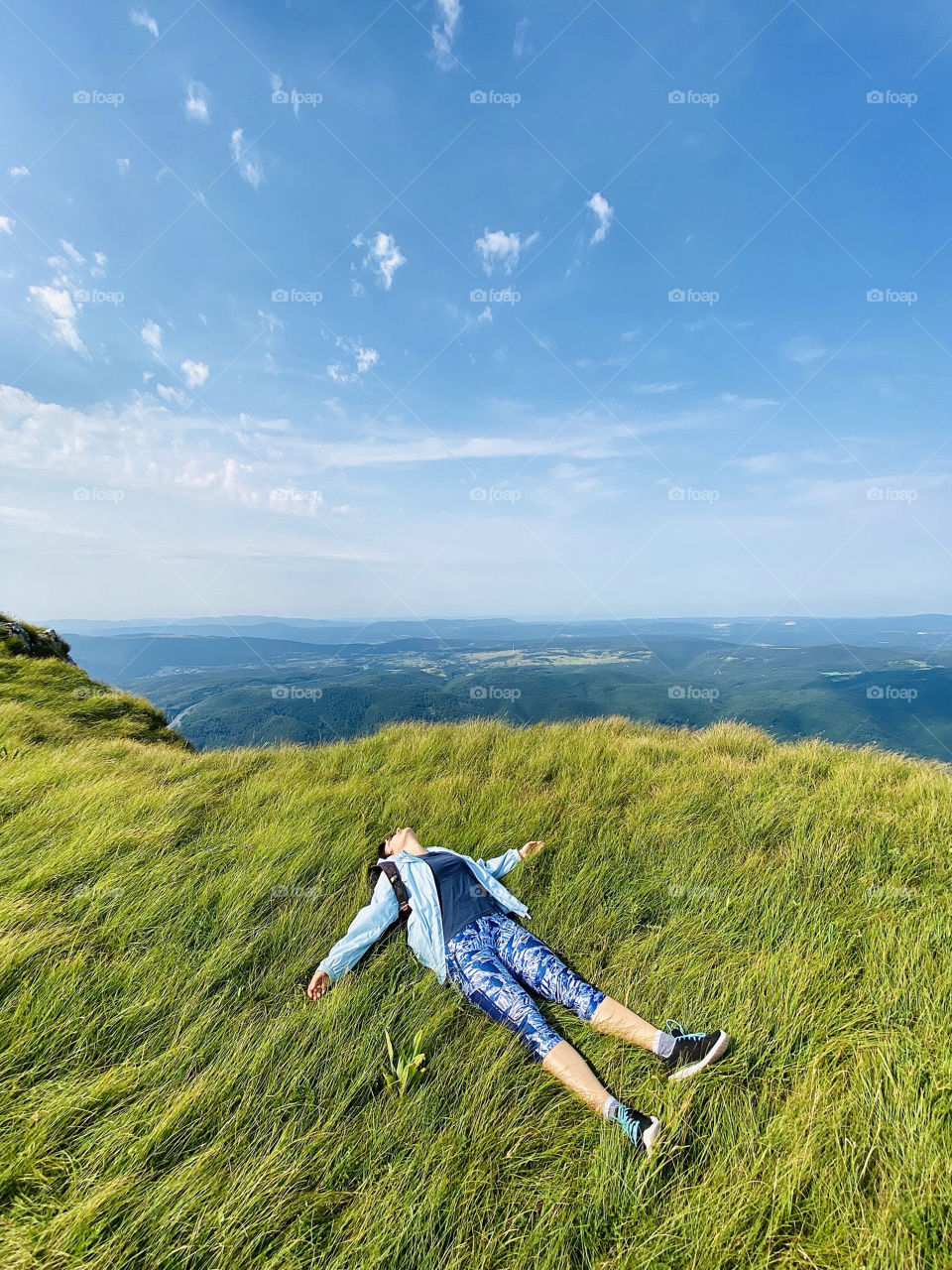 Young active woman, traveler, resting after a steep climb up the mountain.  Lies in the green dense grass on the hill.