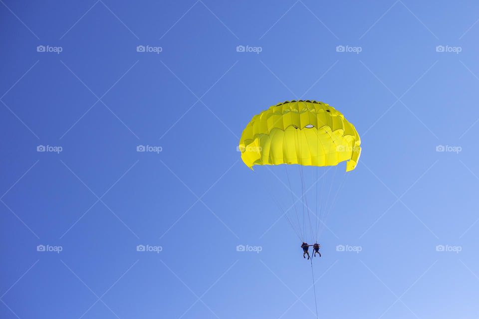 Yellow parachute in the blue sky with two people