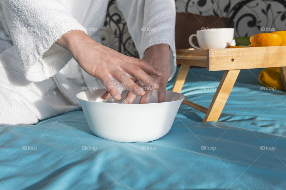 A man at home takes care of himself and does a manicure at home on a blue background and with orange.