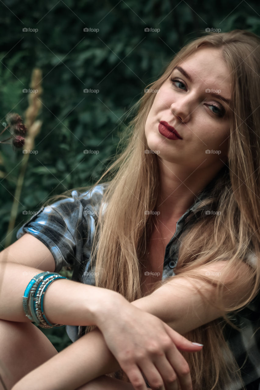 A girl with blond hair in a plaid shirt and short denim shorts on a background of trees and nature Girl, woman, man, people, blonde, blonde hair, checkered shirt, shorts shorts, denim shorts, forest nature, trees, grass, feelings, emotions tenderness, love, lifestyle, lifestyle, recreation