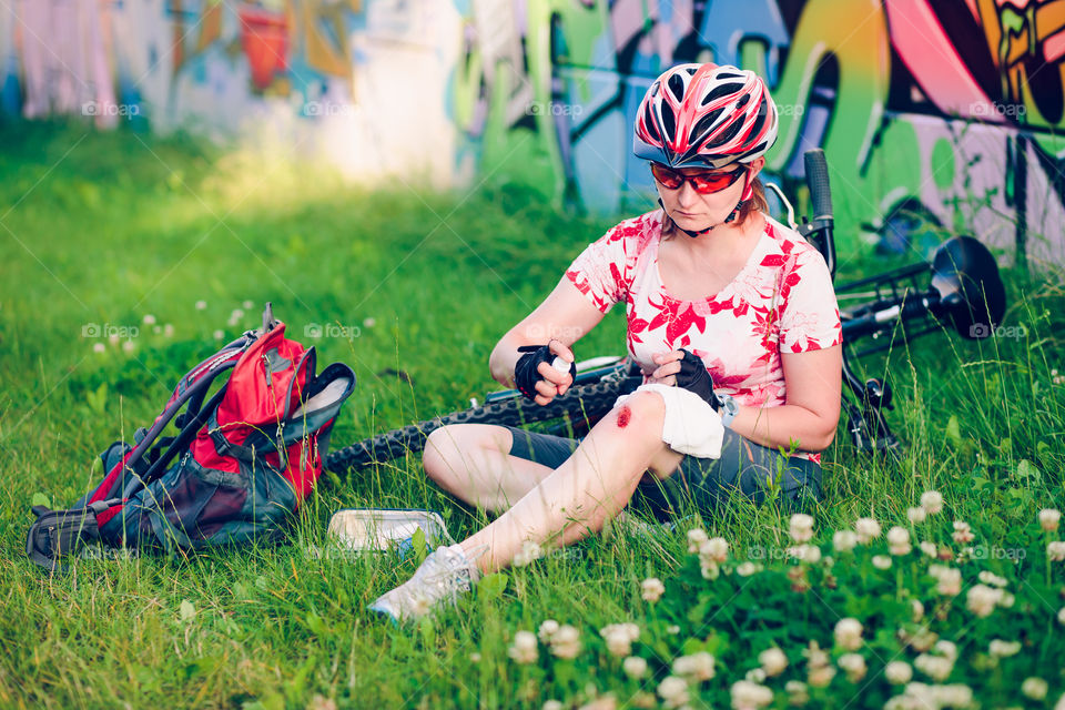 Woman dressing the wound on her knee with medicine in spray and gauze on bike trip on summer day