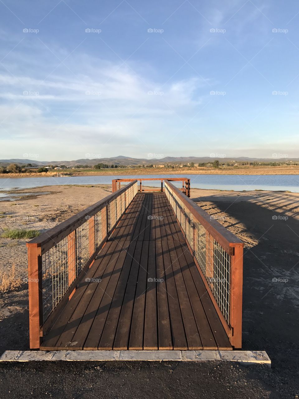 A wooden viewing bridge extends to a pond in a wildlife park outside of Prineville in Crook County in Central Oregon with the golden glow of evening on a fall day. 