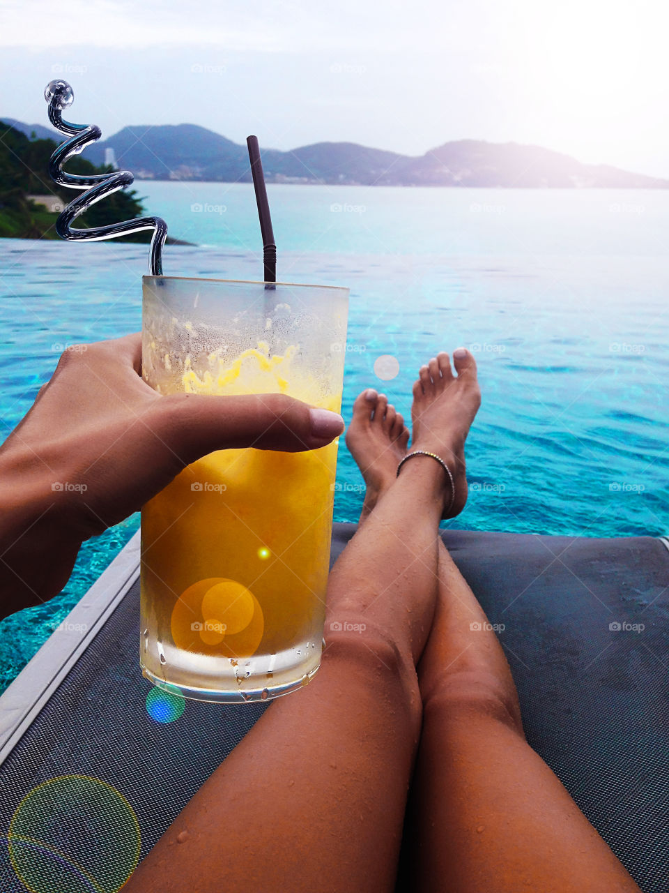 Young woman enjoying her summer tropical cocktail at the swimming pool over the ocean 