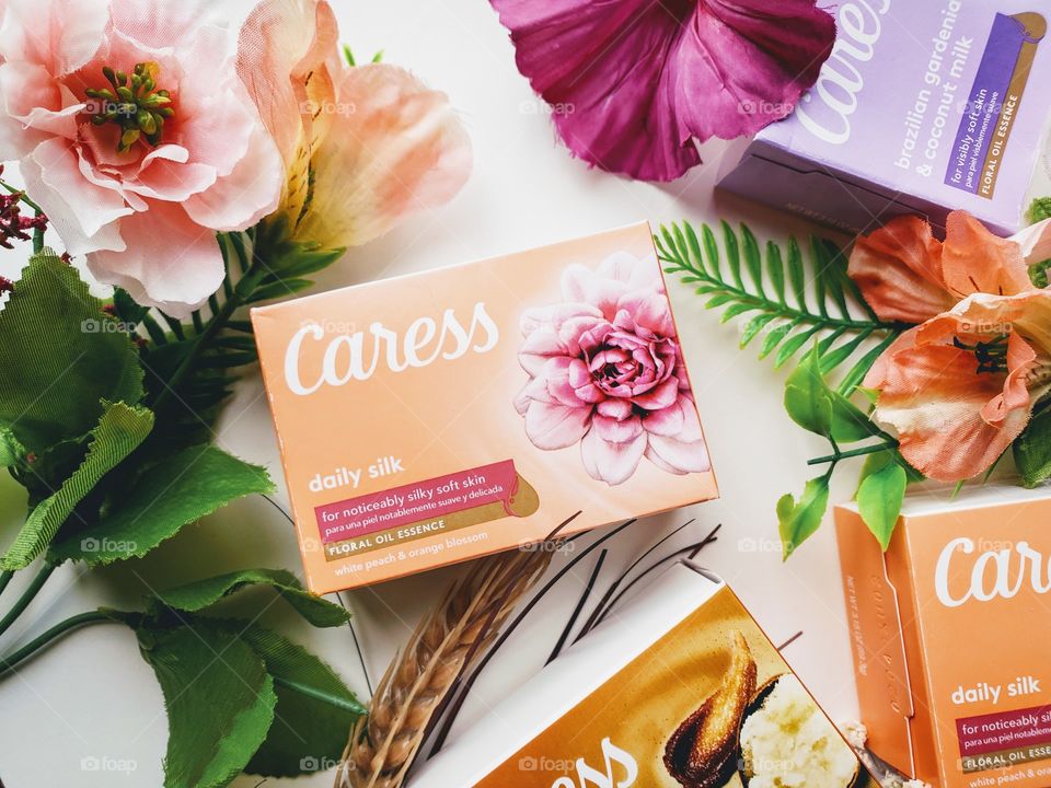 The new look Caress bar single packs: Daily silk, shea butter and brown sugar, and Brazilian gardenia & coconut milk on a white surface surrounded by matching florals.