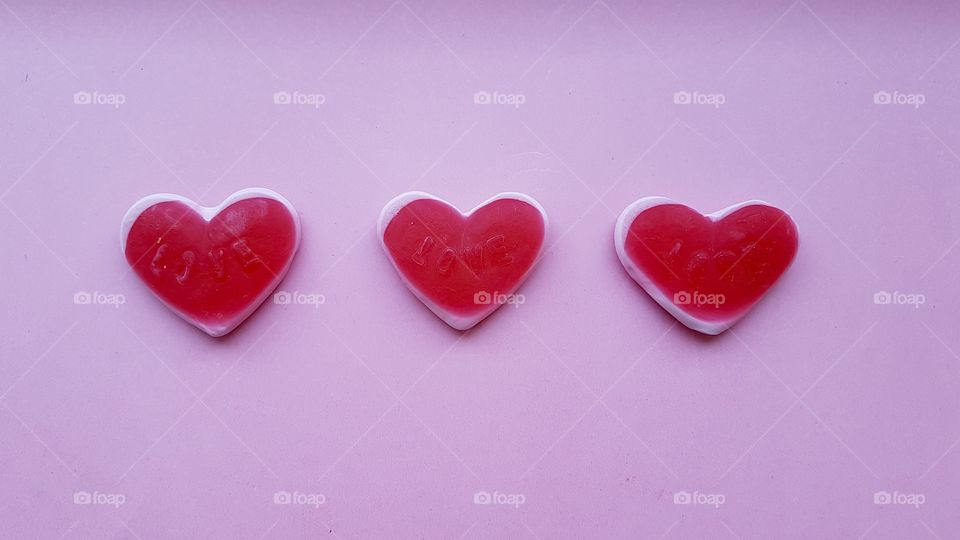 Three red candy hearts on pink background 
