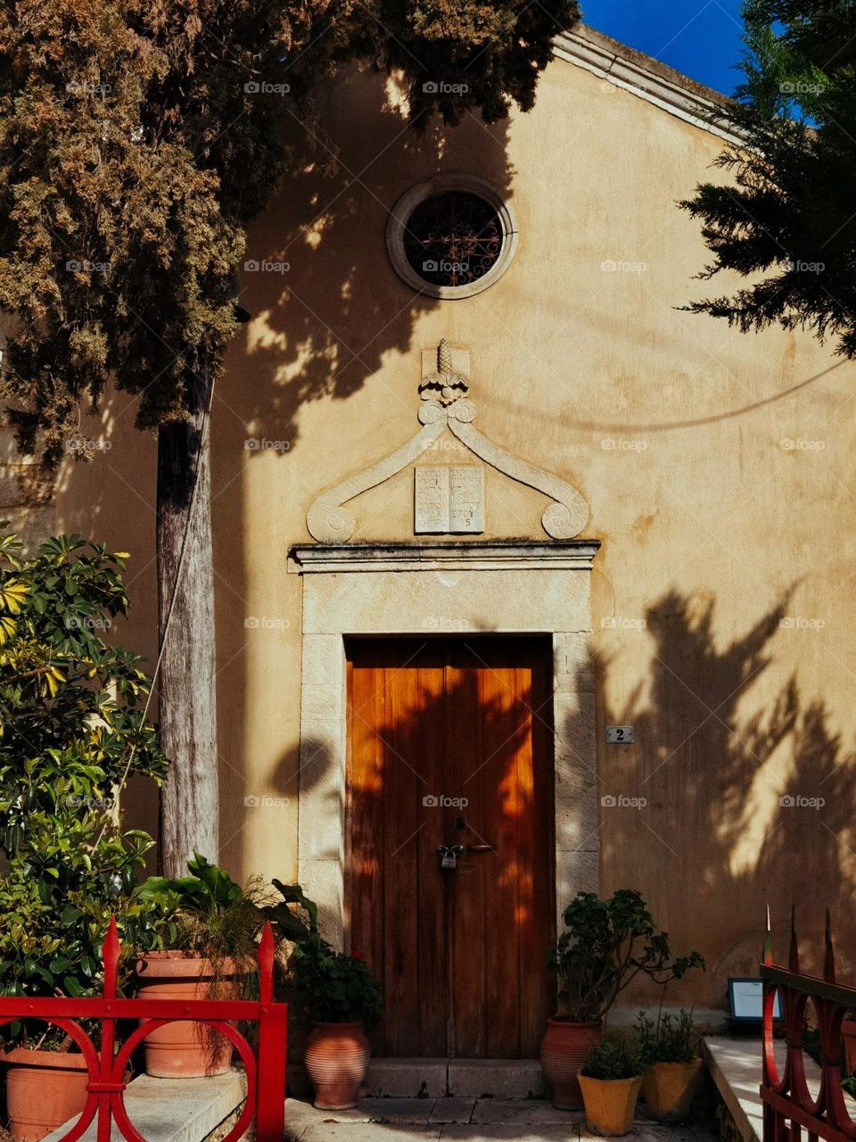 Church in the shadows of trees around clay pots with plants 