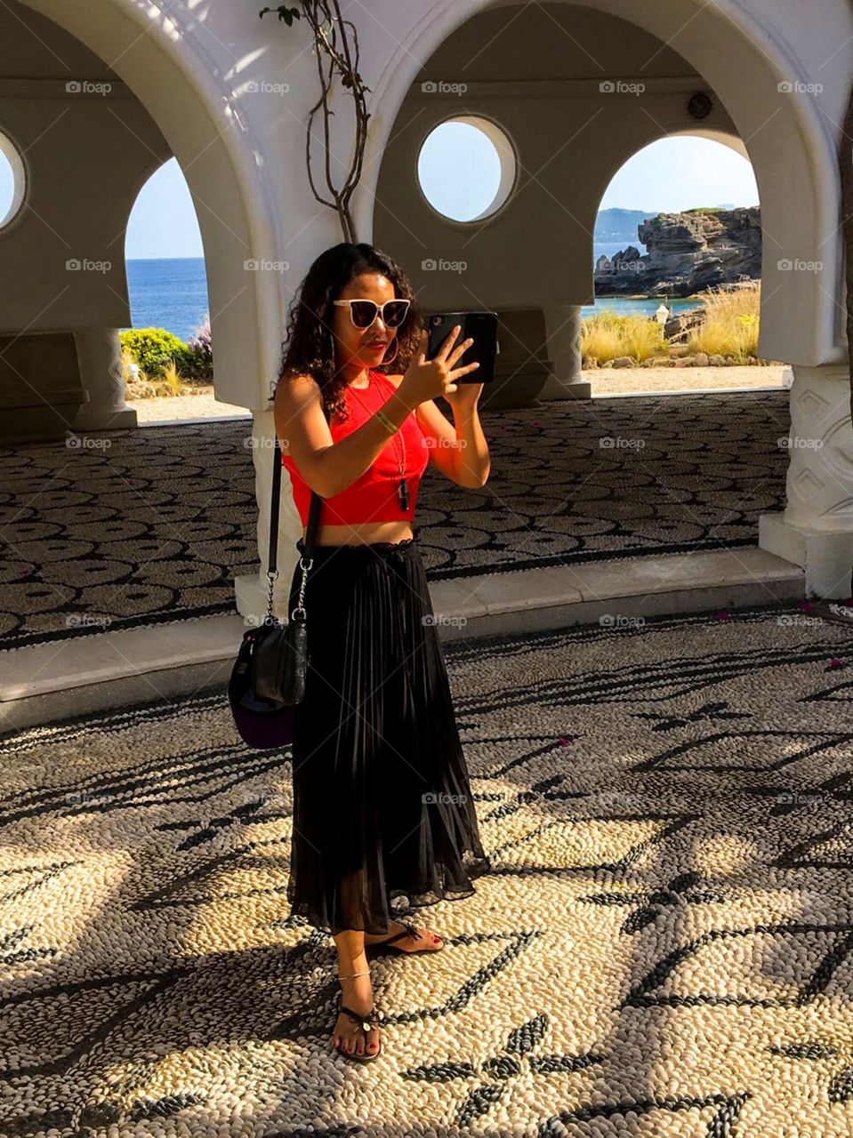 Girl in red shirt, black skirt , black bag, wearing sunglasses on hand holding phone traveling around and taking pictures to keep her moments and memories