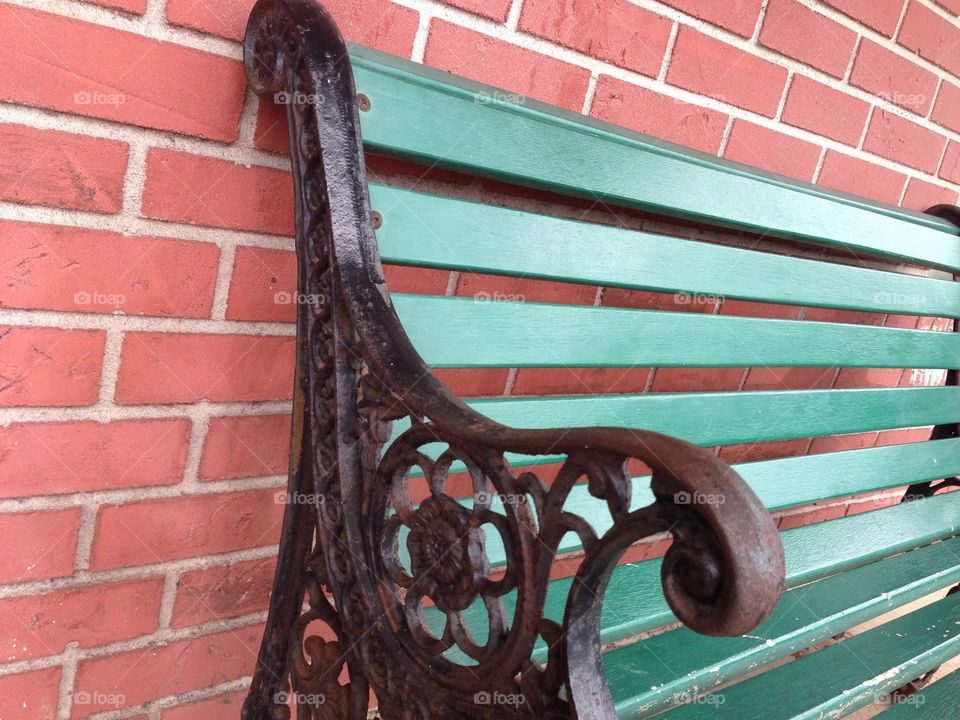 Vintage green bench with iron scrollwork against a red brick wall.