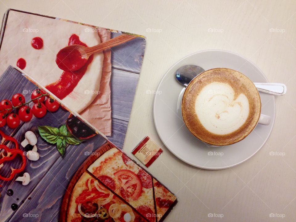 Cap of hot cappuccino and menu on the table 