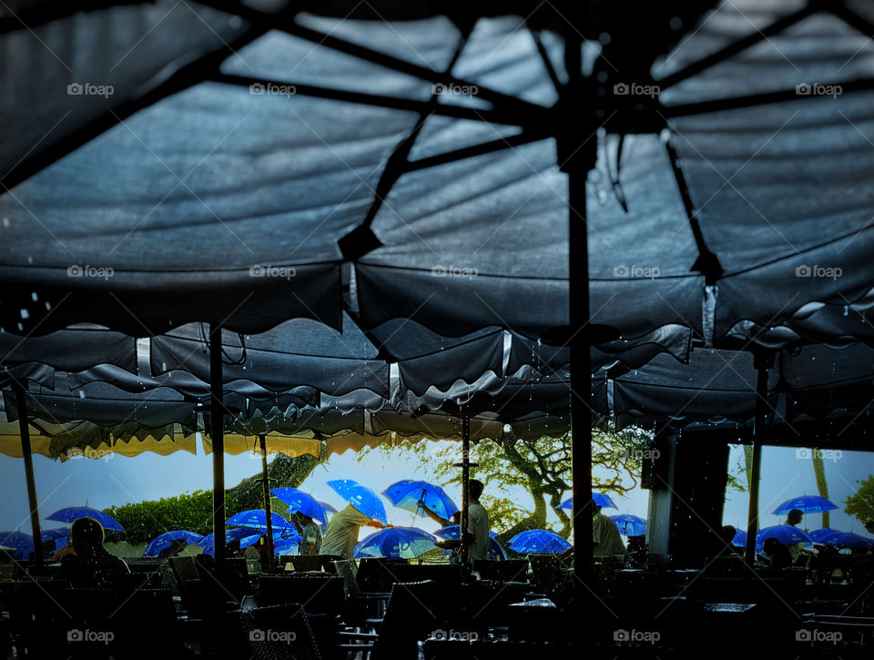Rain falling on an outdoor restaurant where customers open bright blue umbrellas 