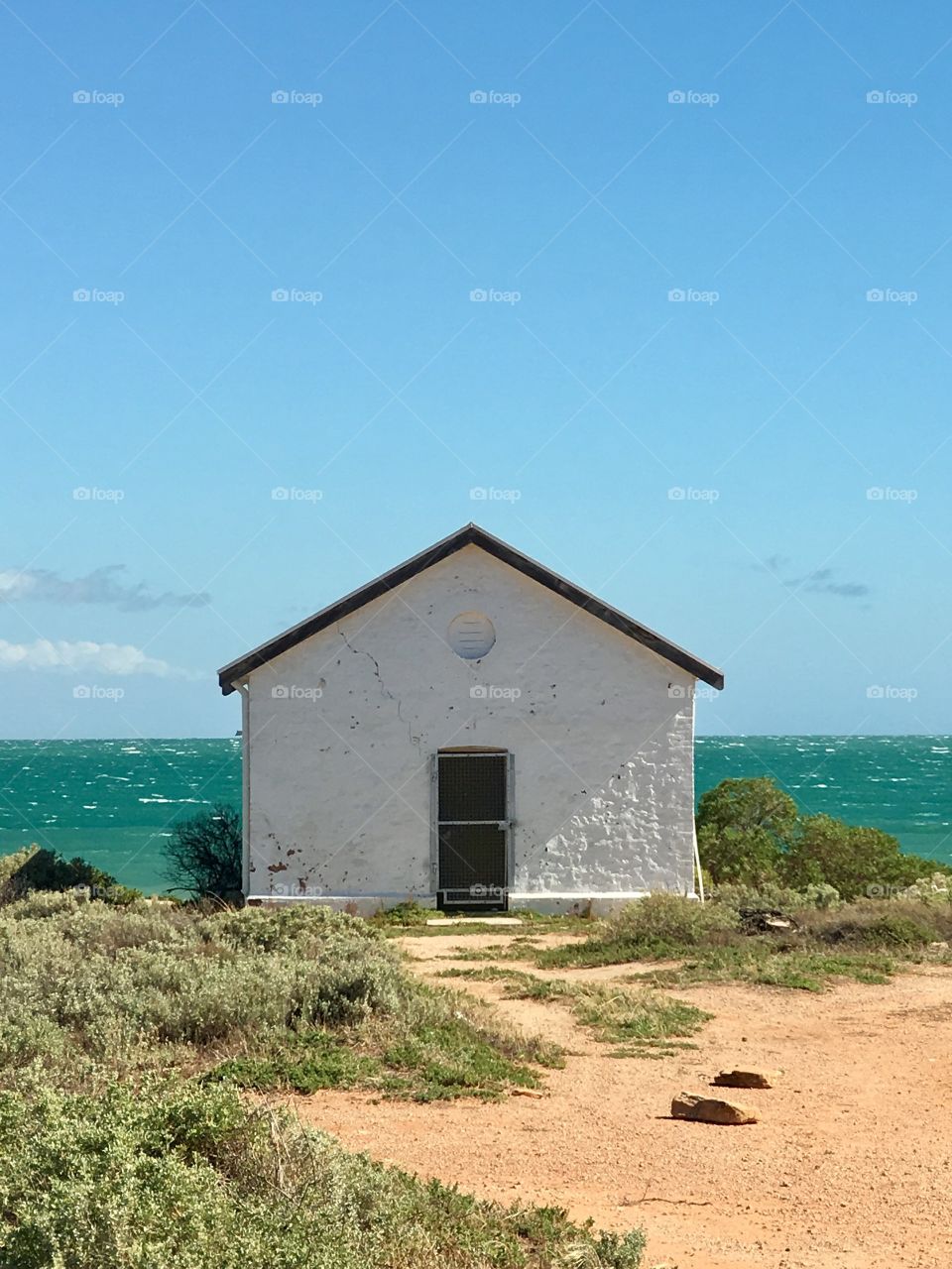 White stone lighthouse keepers cottage house set against ocean horizon on clear blue day, vivid, country seaside charm