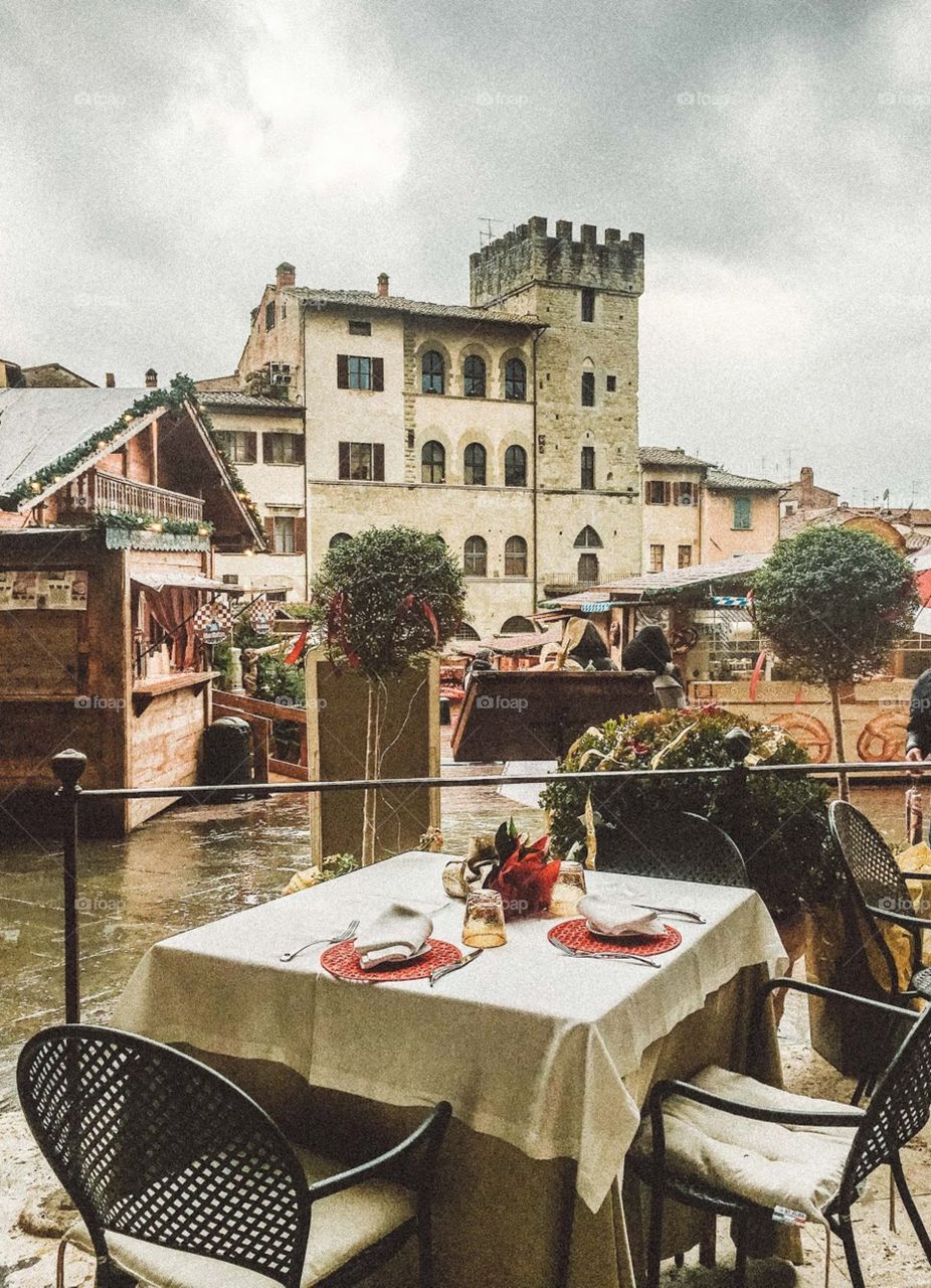 Italian restaurant, view to Piazza Maggiore in Arezzo, medieval towers and market at the square. Table ready.