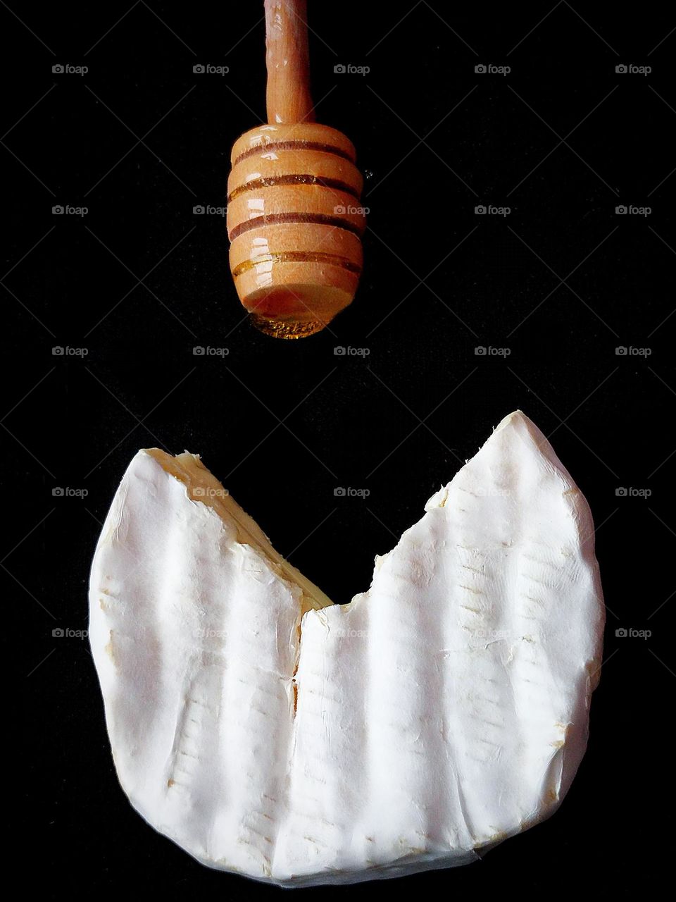 White colour.  On a black background, white Brie cheese, a piece of which is cut off.  From above wooden spoon with yellow honey