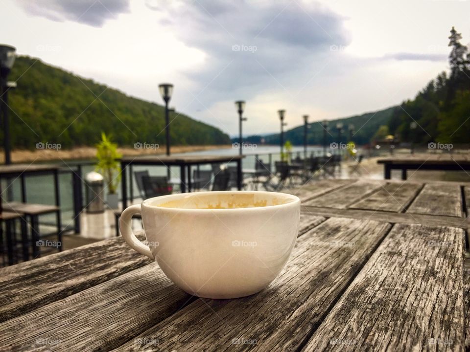 Cup of coffee on wooden table near the lake on a cloudy day