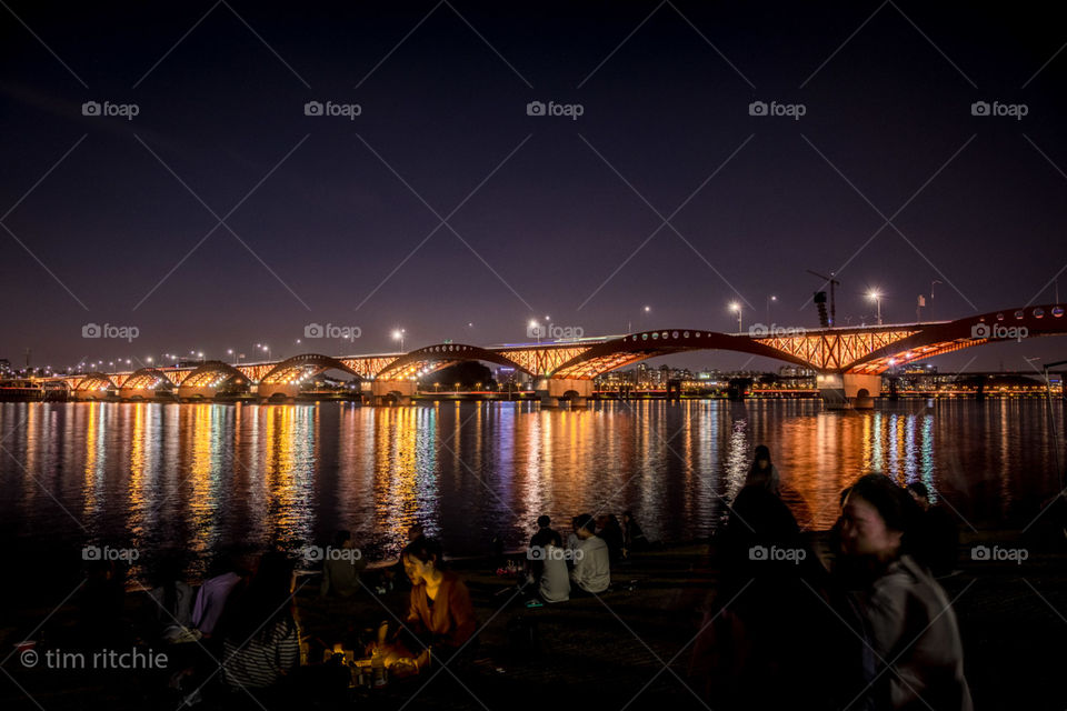 Teams of young woman, and separately  teams of young men, picnic by the Han River in Seoul as the night approaches. This daily ritual in the warmer times often goes unseen by the tourists who stick to the well lit parts of town