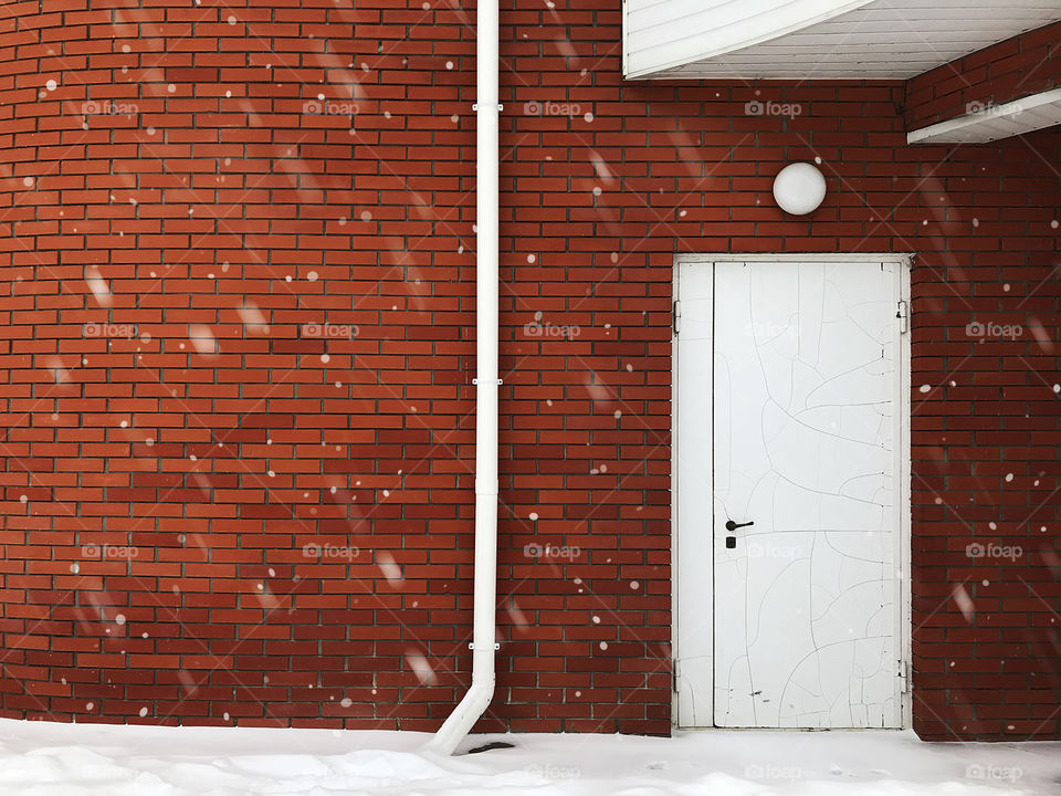 Snowfall in front of white door at the red brick wall 