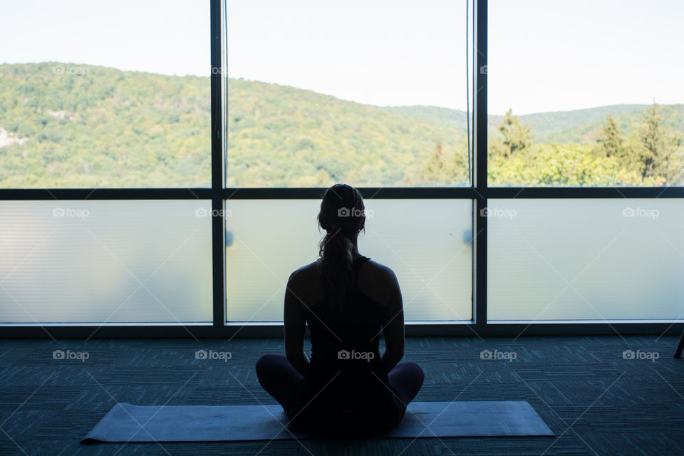 A woman meditates inside towards the window