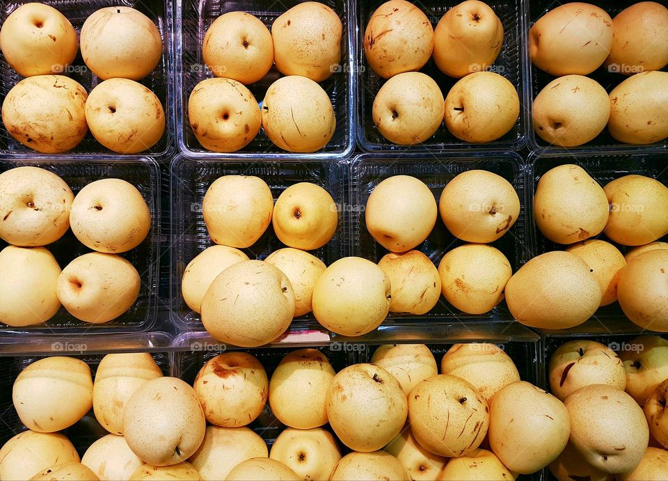 Full frame rows of yellow pears stacked and grouped on display shelves for sale