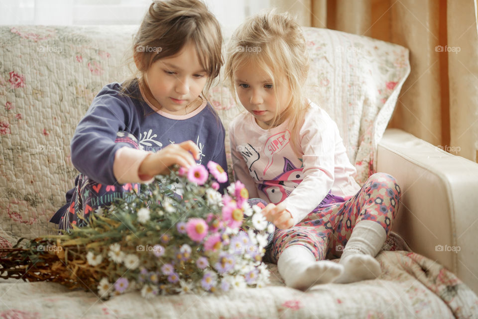 Little sisters in pajamas with bouquet of autumn flowers at home. 