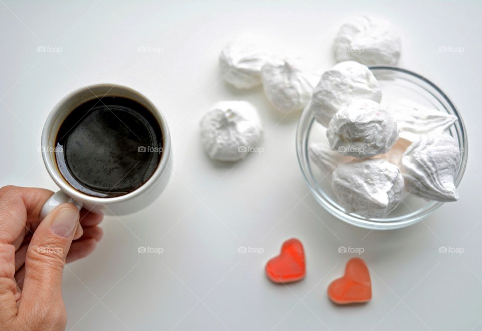 cup of coffee in the hand and sweet sugar meringues on a white background, morning routine