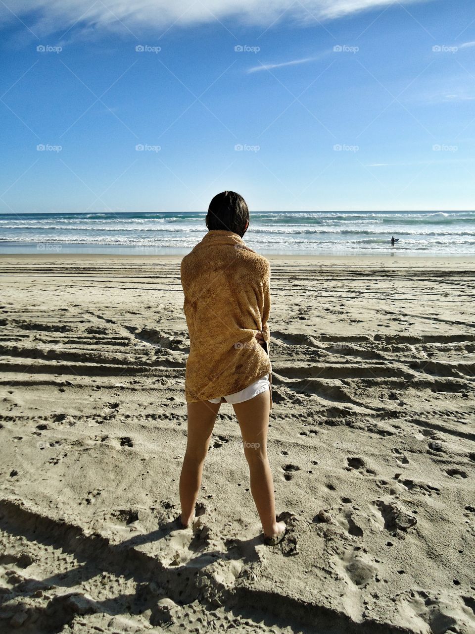 Girl wrapped in beach towel looking out to the ocean waves