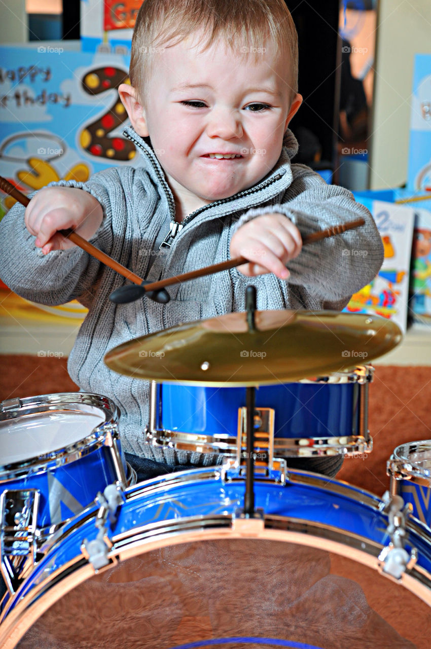 A YOUNG WHITE BOY, AGED THREE, PLAYS A DRUM KIT LIKE A ROCK STAR.