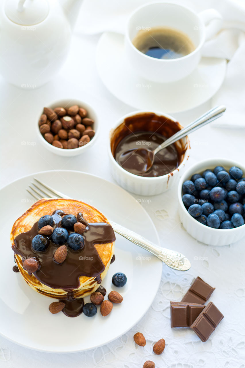 Stack of pancakes with chocolate sauce, blueberries and nuts