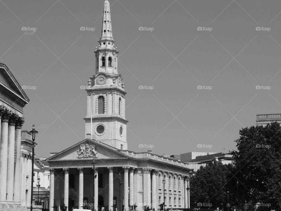 An old ornate building with a clock in its tower, many pillars, and decorative carvings on a sunny summer day in London. 