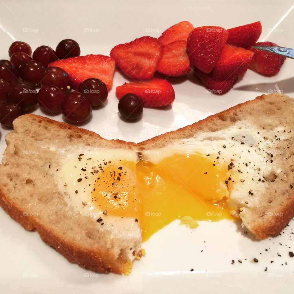 Sunny side Eggs on light multigrain bread seared on a pan. Enjoyed with strawberries and grapes