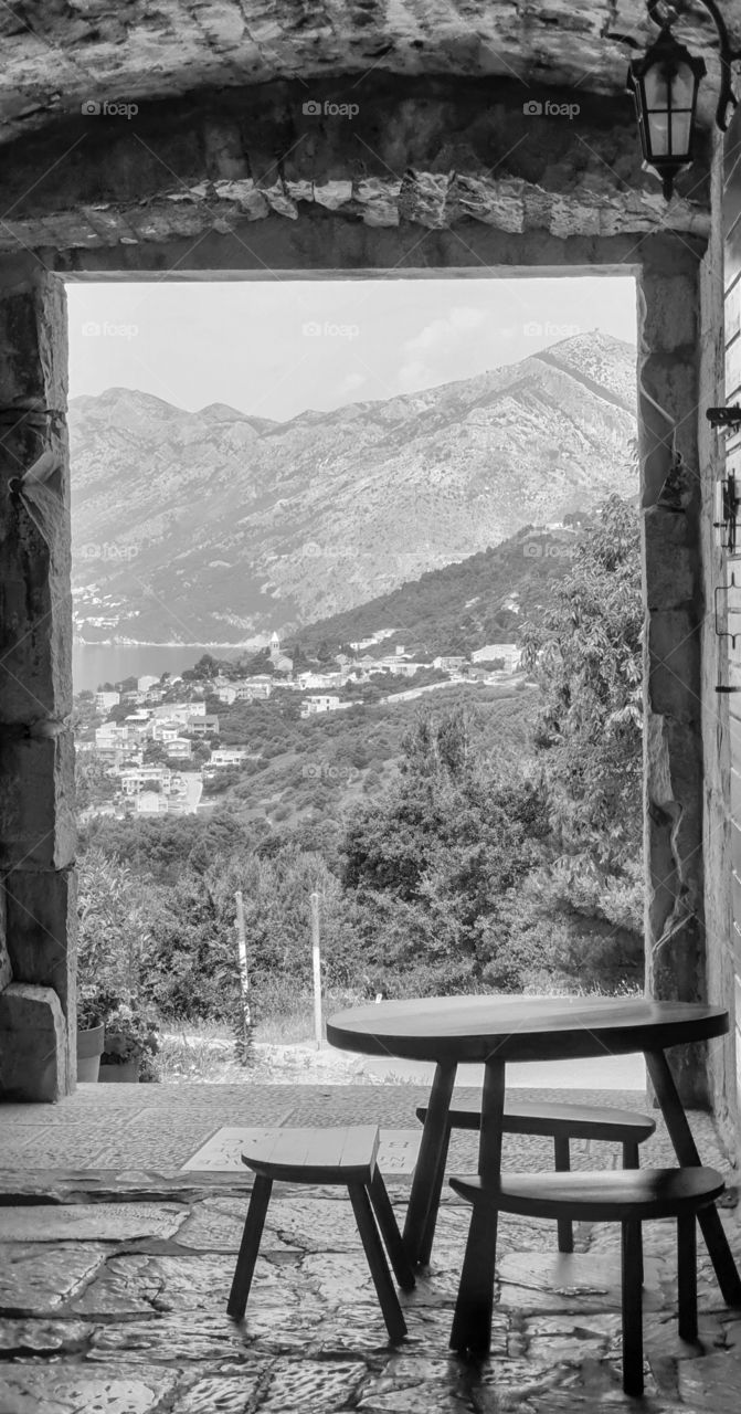 Wooden table and chairs in an outdoor cafe in the old Dolmatian city with stone walls and picturesque summer views of the small old coastal town, olive gardens, sea and mountains.  Summer holidays in the old European Mediterranean town