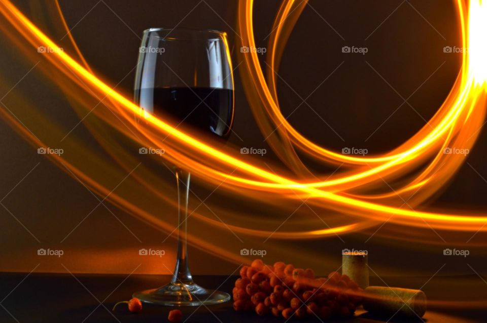 A glass of red wine and rowan berries on a dark background.  4 second exposure shows lines of light around the glass.