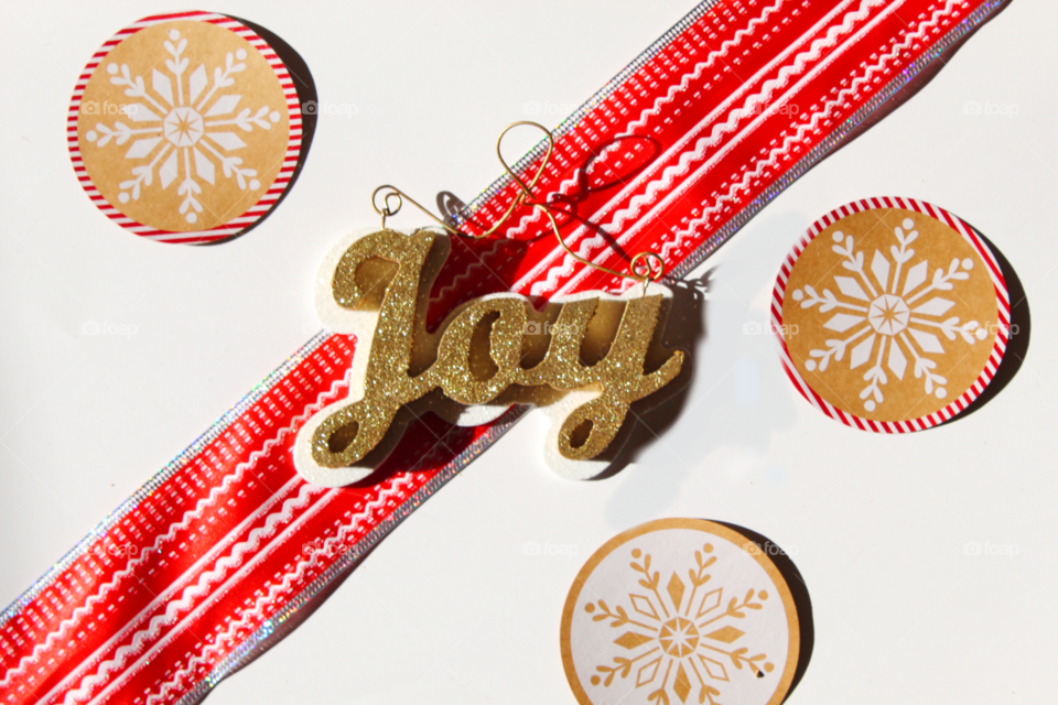 A joy Christmas decoration sits on a red Christmas ribbon surrounded by paper snowflakes