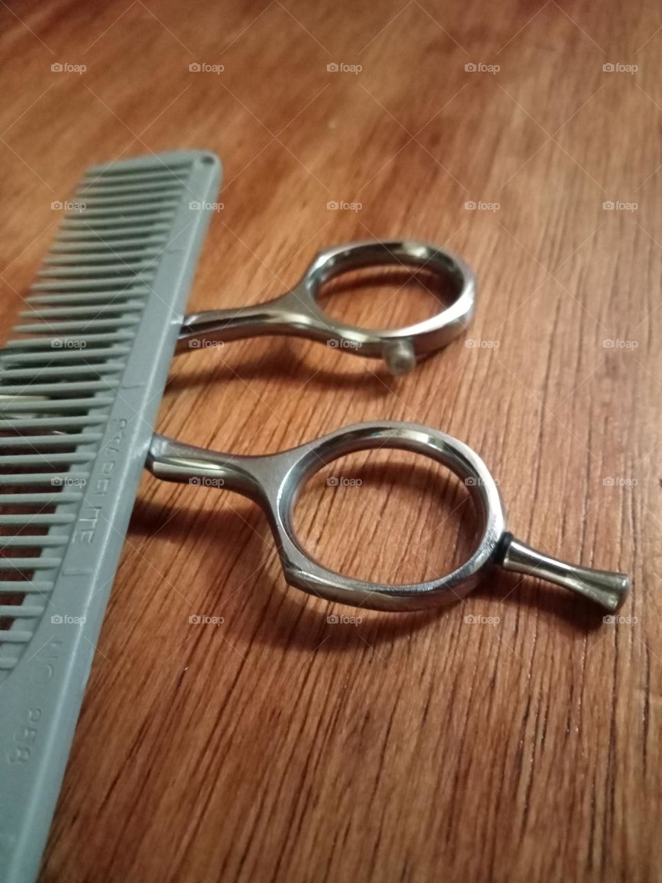 A pair of cutting tools, comb and scissor on the table.