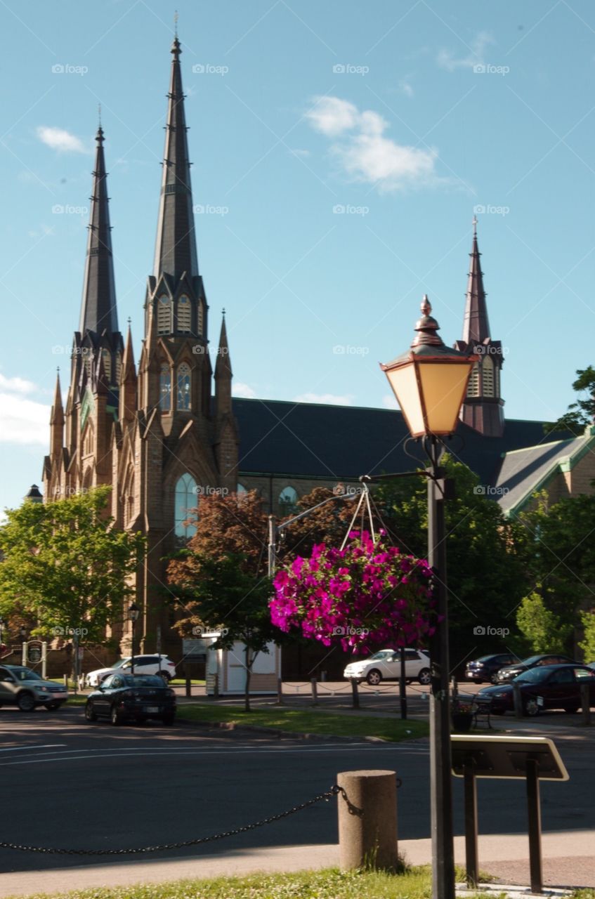 Exterior daylight.  Prince Edward Island.  Foreground: Old fashioned streetlight hangs pink petunias.  Background:  gothic inspired church with spires.