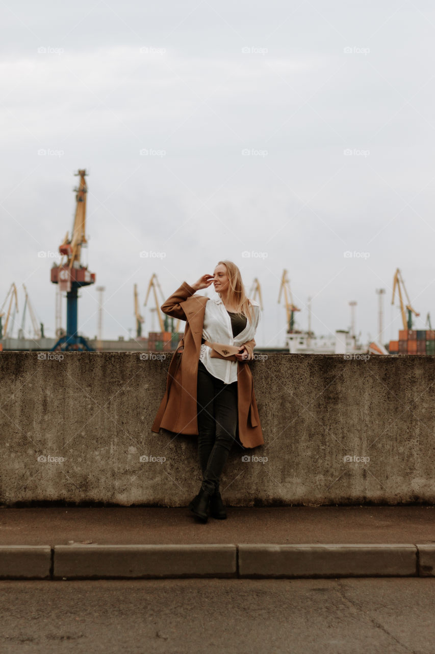 Blonde beautiful girl standing in a camel coat in a port