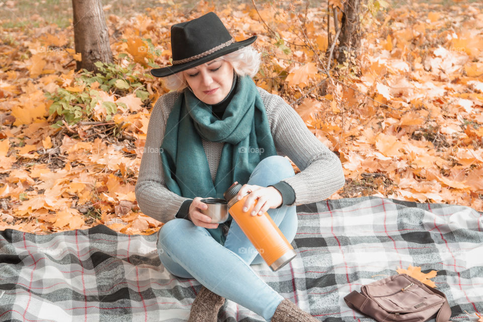 Portrait of middle aged adult woman in a knitted jumper and black hat relaxing in autumn forest