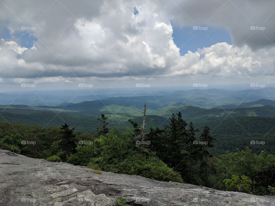 the view from atop a boulder on the Blue Ridge Parkway, North Carolina. Clouds in the sky over a forested hiking trail in the valley.