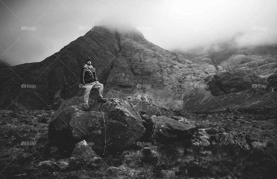 A man stands atop of large boulders in a misty mountainous landscape 