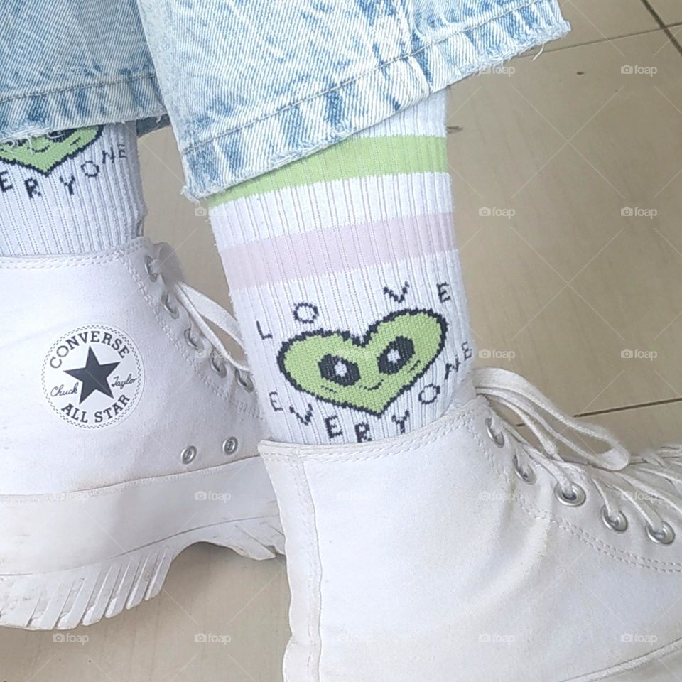 A young person is wearing Converse brand sneakers and jeans. The focus is on the socks in the center of the photograph with an important "love everyone" message and the colors pink and green.