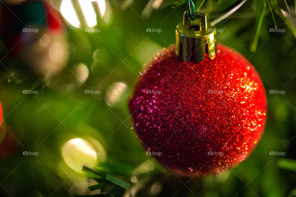 A bright red sparkling Christmas ornament hanging on a tree with nice deep green bokeh and blurred lights. Looks like a greeting card.