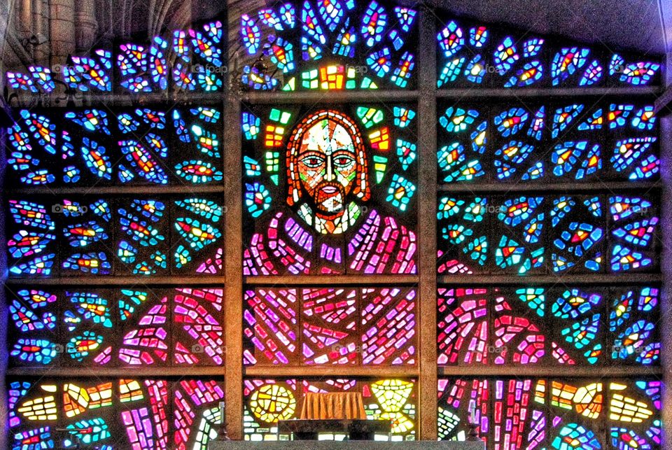 A stained glass window of Jesus Christ with his arms open wide.