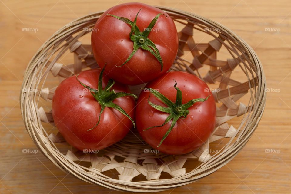 Fresh tomatoes in a wicker plate on a wooden background. Collection of tomatoes. View from above