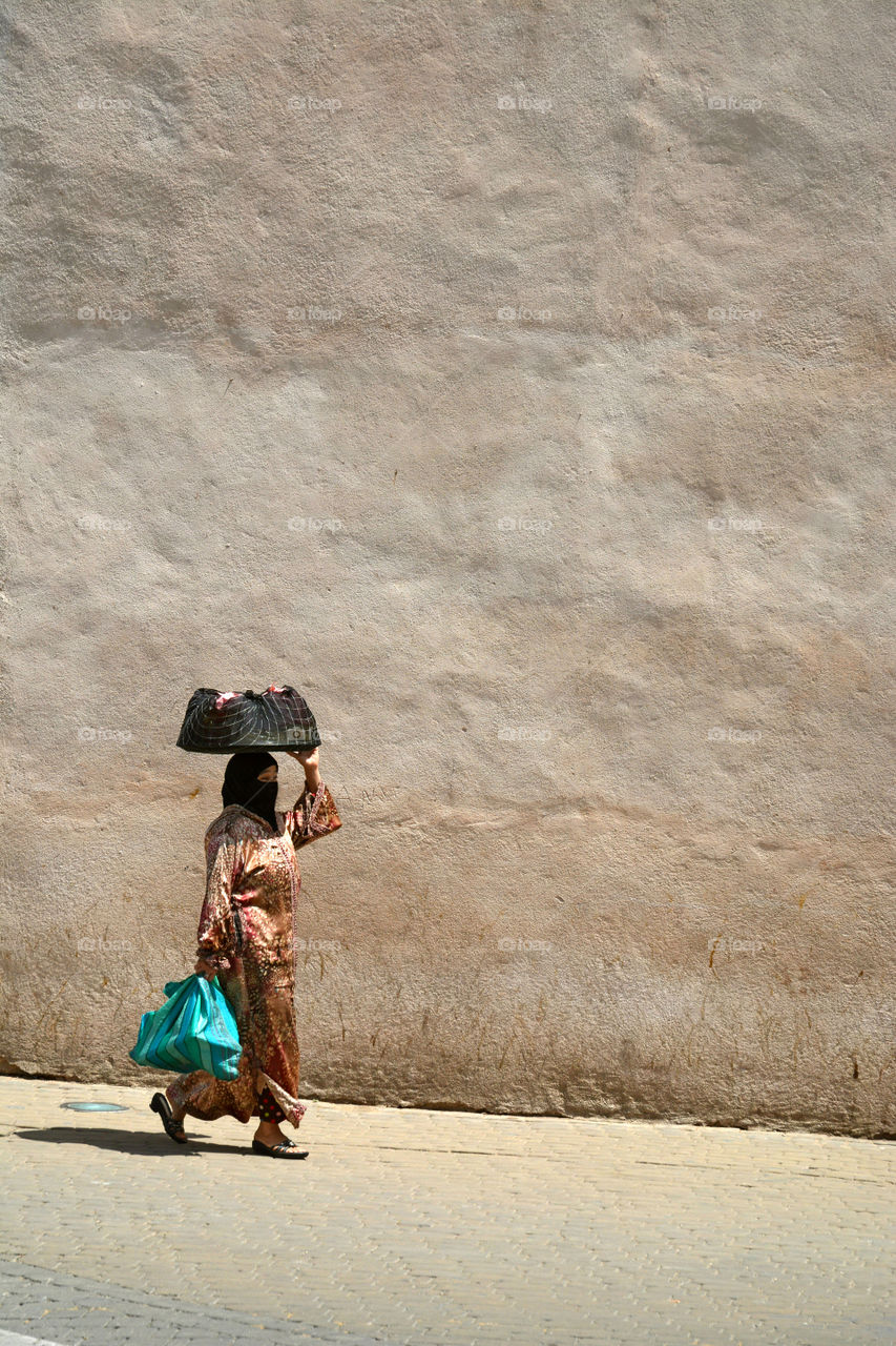 Islam woman is shopping and walking before a old city wall in Marocco