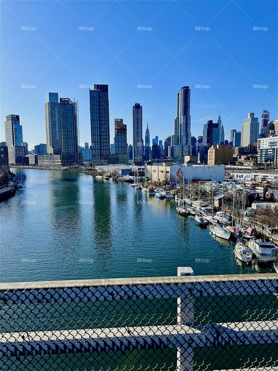 This is beautiful „Newtown Creek“ with its great variety of boats seen from the „Pulaski Bridge“ that connects „Greenpoint“, Brooklyn to LIC, Queens. In the distance straight ahead we can see „Manhattan“. 2024. Hypnotic Productions
