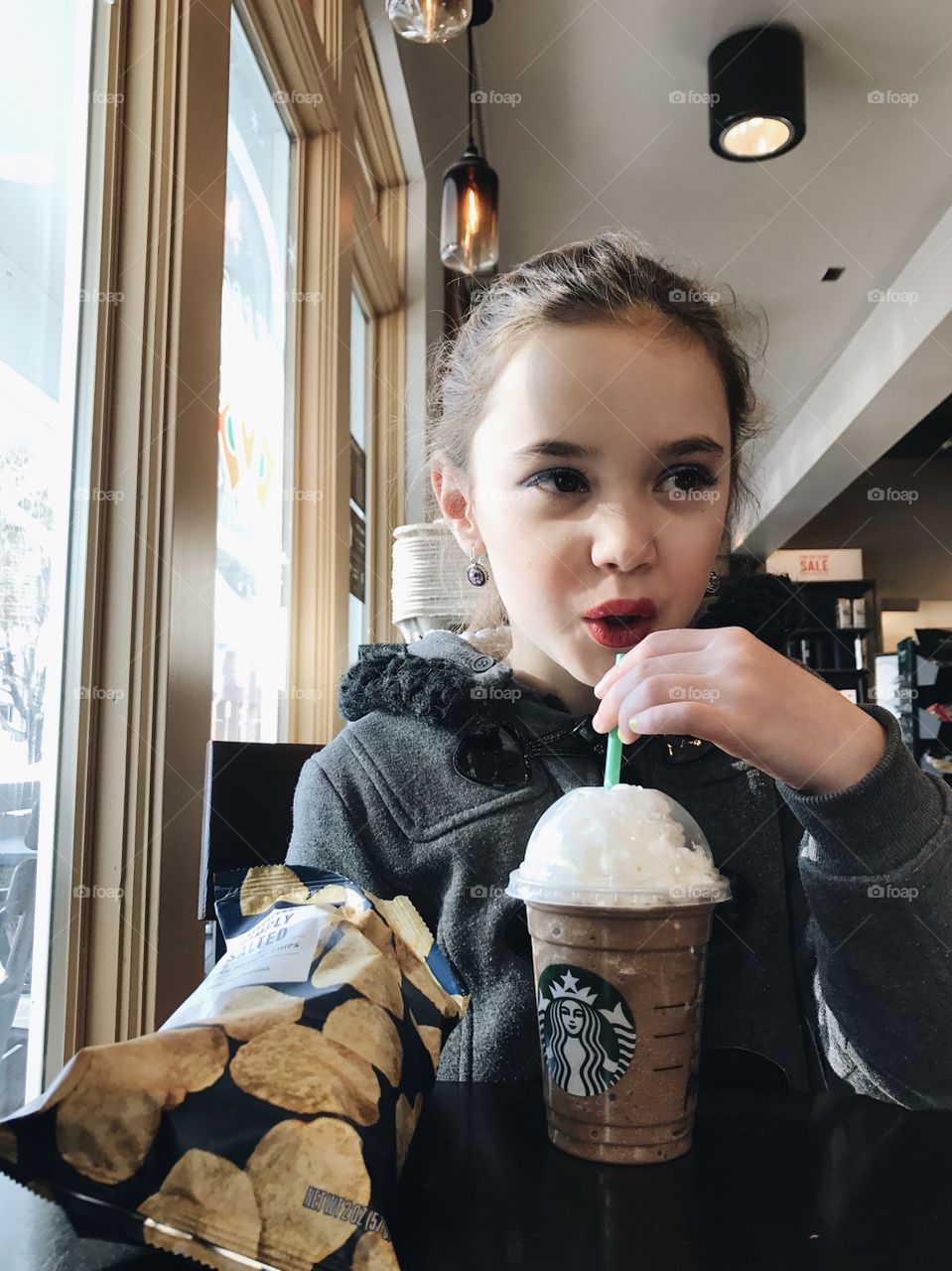 Cute, little girl out on a Starbucks Frappuccino date with her momma in a warm coat by the window. 