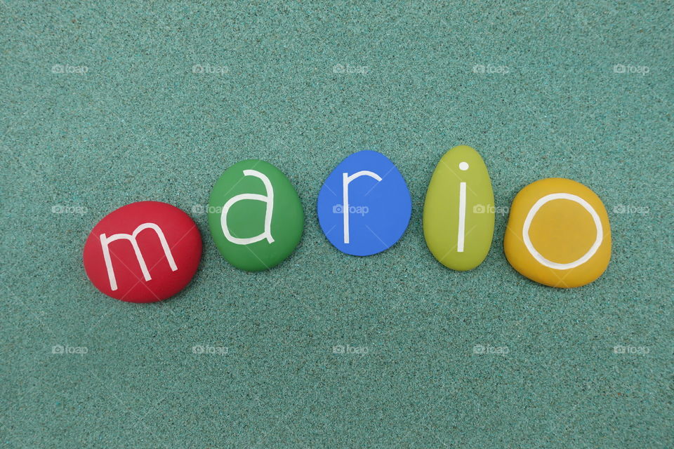 Mario, masculine given name composed with colored stones over green sand 