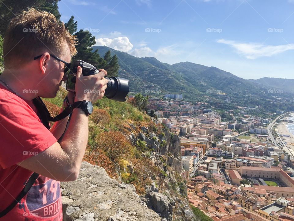 Male tourist taking picture of the town Cefalu high up on a mountain on Sicily.