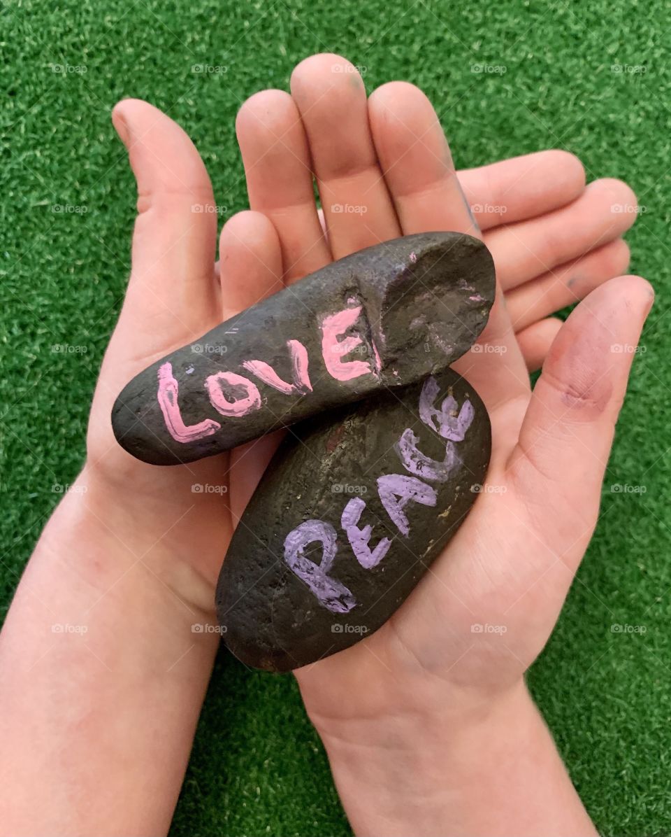 Child holding black rocks with words love and peace painted on the rocks 
